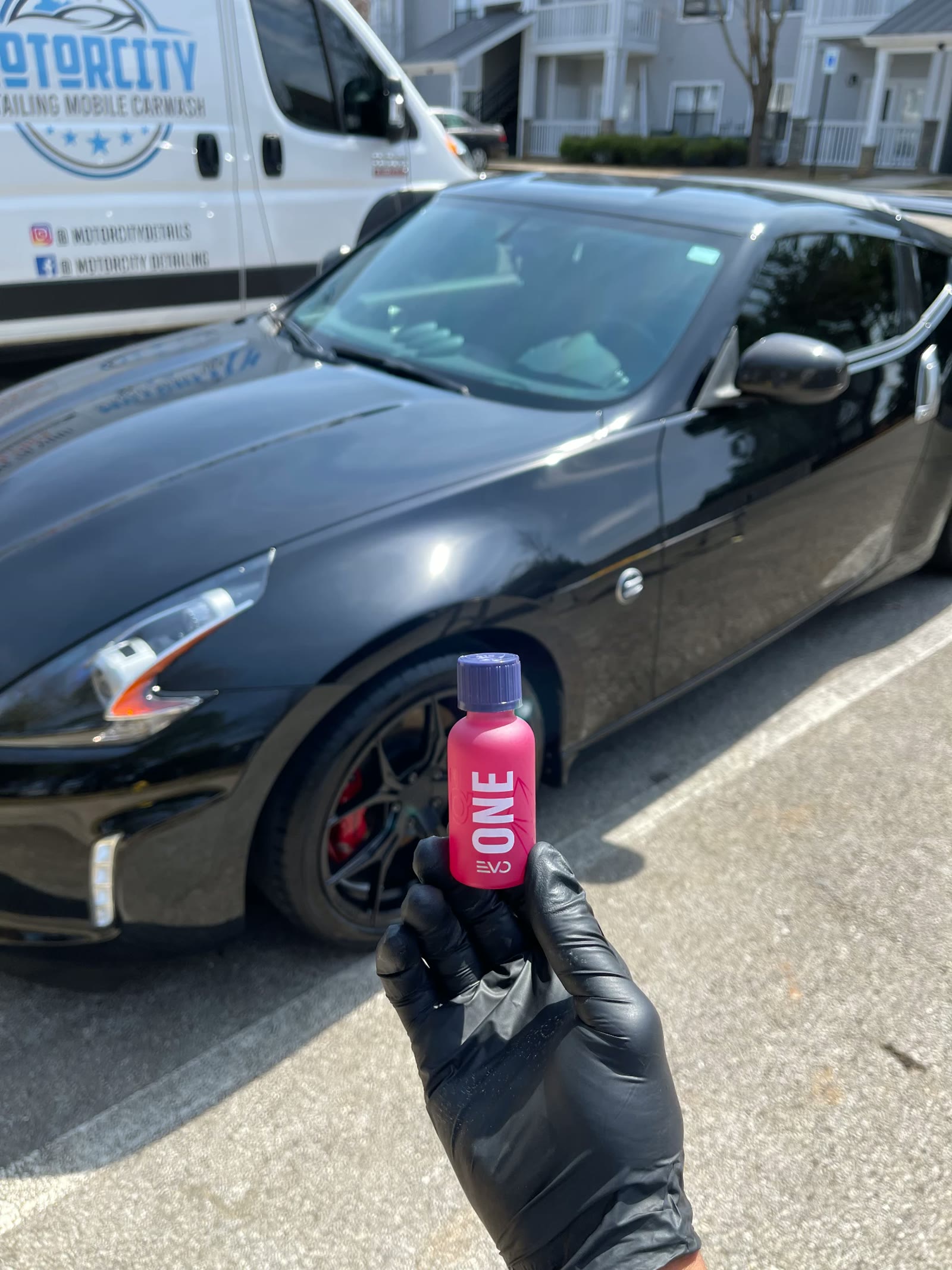 Detailer holding a bottle of GYEON coating next to a black Nissan 370Z and the Motorcity mobile unit
